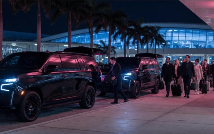 Black SUVs and a group with luggage arriving outside an airport terminal at night